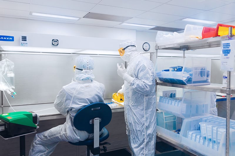 Two professionals in a laboratory working wearing protective suits