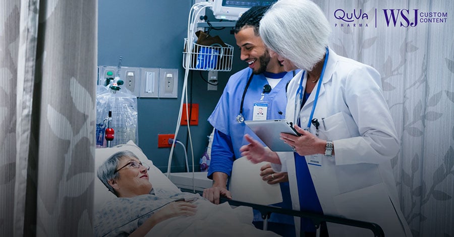 Two health professionals check a patient in a hospital bed