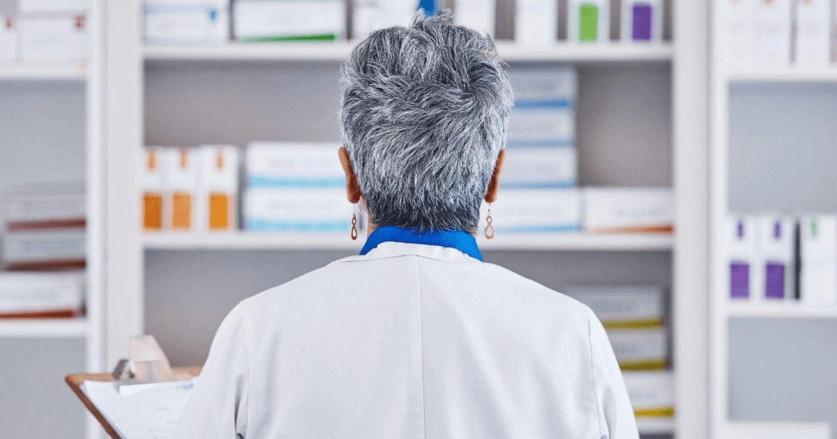 pharmacist is seen with her back towards the camera, facing a shelf